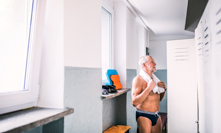 Senior man standing by the lockers in an indoor swimming pool.の写真素材
