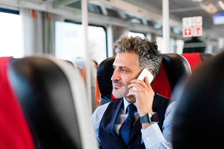Mature businessman with smartphone travelling by train.の写真素材