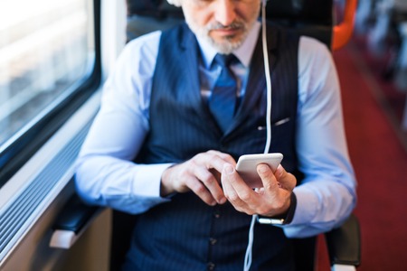 Mature businessman with smartphone travelling by train.