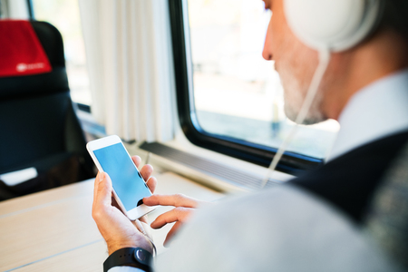 Mature businessman with smartphone travelling by train.の写真素材