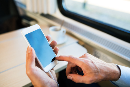 Mature businessman with smartphone travelling by train.の写真素材