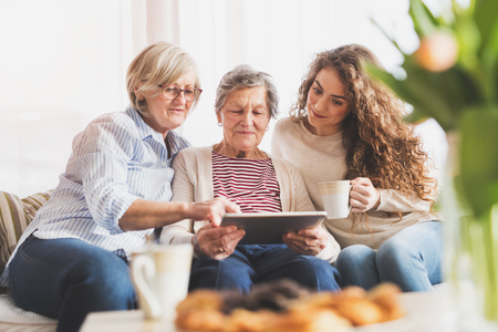 A teenage girl, mother and grandmother with tablet at home.
