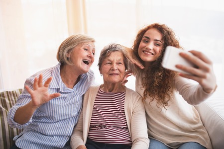 A teenage girl, mother and grandmother with smartphone at home.の写真素材