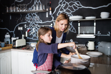 A small girl with her mother cooking at home.の写真素材