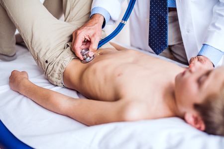 Senior doctor examining a small boy in his office.の写真素材