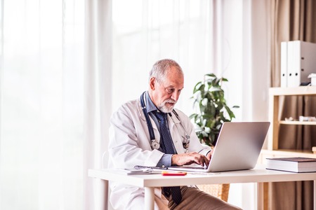 Senior doctor with laptop working at the office desk.