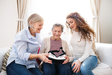A teenage girl, mother and grandmother with VR goggles at home.の写真素材