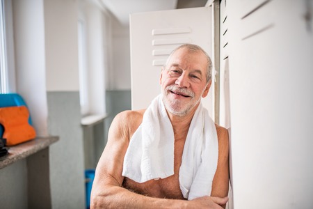 Senior man standing by the lockers in an indoor swimming pool.の写真素材