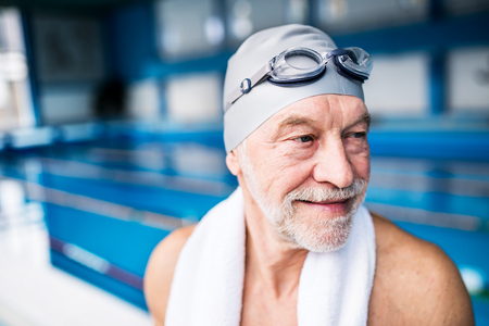 Senior man standing in an indoor swimming pool.の写真素材