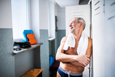 Senior man standing by the lockers in an indoor swimming pool.の写真素材