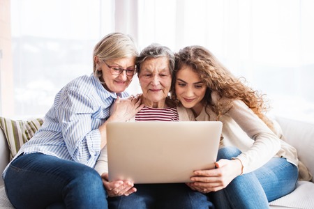 A teenage girl, mother and grandmother with laptop at home.の写真素材