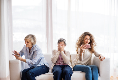 A teenage girl, mother and grandmother with smartphone at home.の写真素材