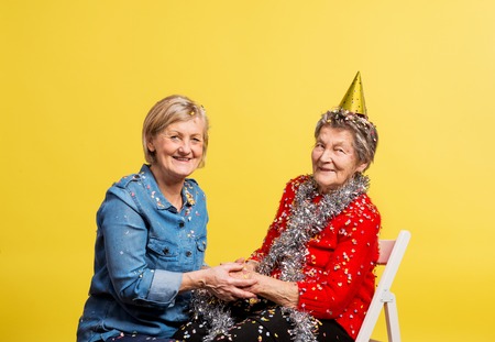 Portrait of a senior women in studio on a yellow background. Party concept.の写真素材