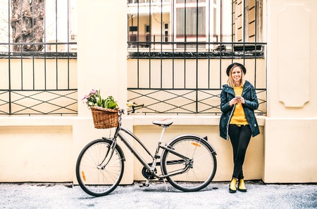 Young woman with bicycle and smartphone in sunny spring town.の写真素材