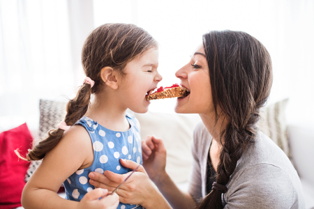 Young mother with a small girl at home, eating.の写真素材