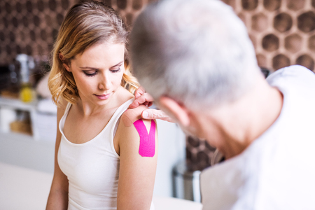 Senior male physiotherapist applying tape on a female patient.の写真素材