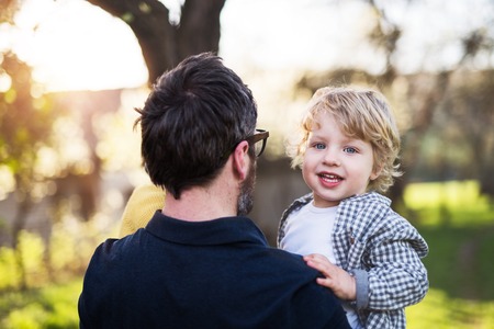 A father holding his toddler son outside in spring nature.の写真素材