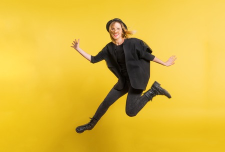 Young beautiful woman with black hat in studio on a yellow background, jumping.