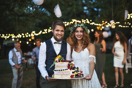 Bride and groom holding a cake at wedding reception outside in the backyard.の写真素材