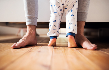 Legs of father and a toddler boy standing on the floor in bedroom at home.の写真素材
