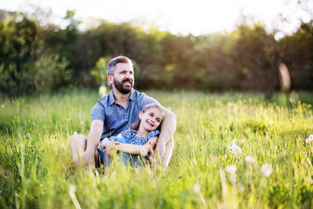 Father with a small daughter sitting on the grass in spring nature.の写真素材
