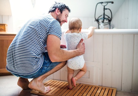 Father with a toddler child at home standing by the tub in the bathroom.の写真素材