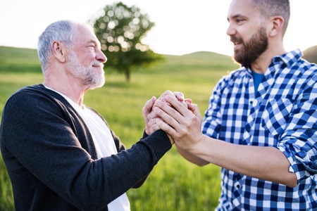 An adult hipster son with senior father on a walk in nature at sunset.の写真素材