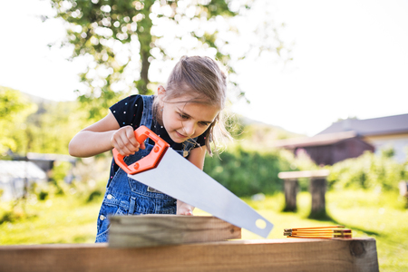 A small girl with a saw outside, making a wooden birdhouse.の写真素材