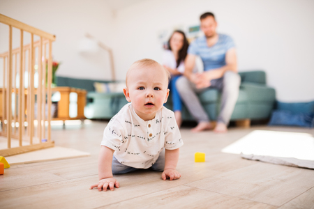 A baby boy crawling on the floor at home, parents in the background.の写真素材