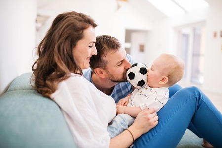Young family with a baby boy at home, sitting on the sofa.