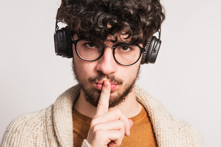 Portrait of a young man with headphones in a studio, finger on his mouth.の写真素材