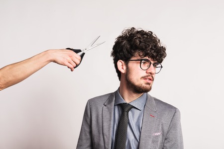 Portrait of a young man in a studio and a hand with scissors.の写真素材