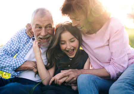 Senior couple with granddaughter outside in spring nature, relaxing on the grass.の写真素材
