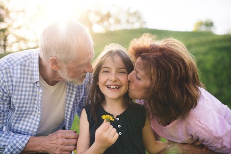 Senior couple with granddaughter outside in spring nature, relaxing on the grass.の写真素材