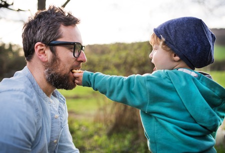 A toddler boy giving his father a biscuit outside in spring nature.の写真素材