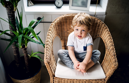 A toddler boy sitting on the wicker chair in the bathroom at home.の写真素材