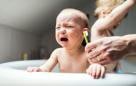 An unhappy baby girl with unrecognizable father crying when brushing teeth.の写真素材