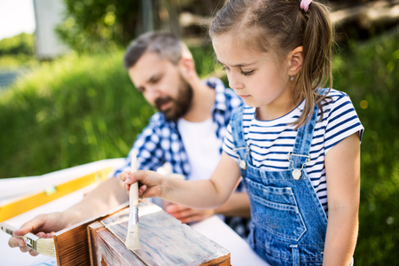 Father with a small daughter outside, painting wooden birdhouse.の写真素材