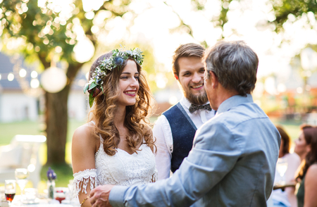 A senior father congratulating bride and groom at wedding reception outside in the backyard.の写真素材