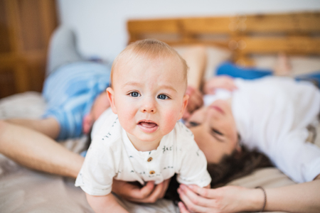 A baby boy at home on bed with unrecognizable parents.の写真素材