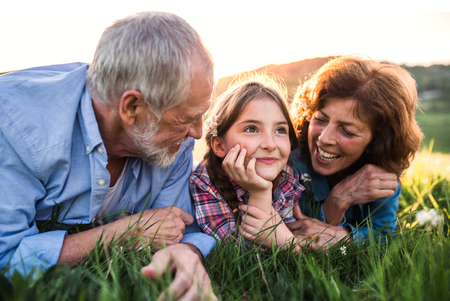 Senior couple with granddaughter outside in spring nature, relaxing on the grass.の写真素材