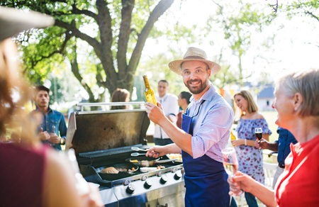 A mature man with family and friends cooking and serving food on a barbecue party.の写真素材