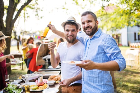 Portrait of two men on a family celebration or a barbecue party outside in the backyard.の写真素材