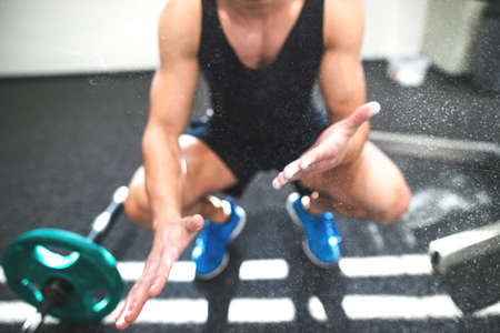 Fit young man in gym with barbells smearing his hands with magnesium.の写真素材