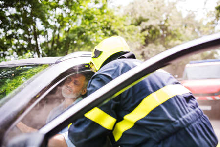A firefighter getting an unconscious man out of the car after an accident.の写真素材