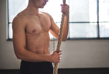 Fit young man in gym standing topless , holding climbing rope.の写真素材