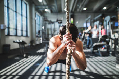 Fit young man in gym working out with climbing rope.の写真素材