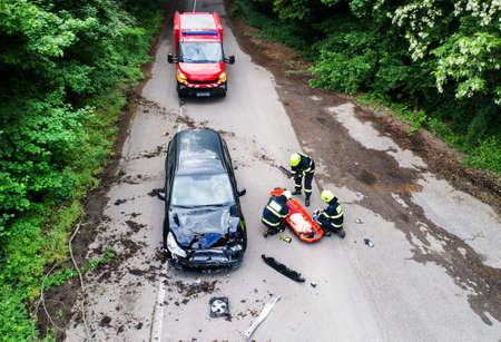 Three firefighters helping a young injured woman lying on the road after an accident.の写真素材