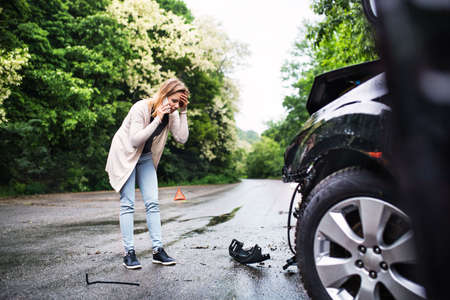 Young woman by the damaged car after a car accident, making a phone call.の写真素材