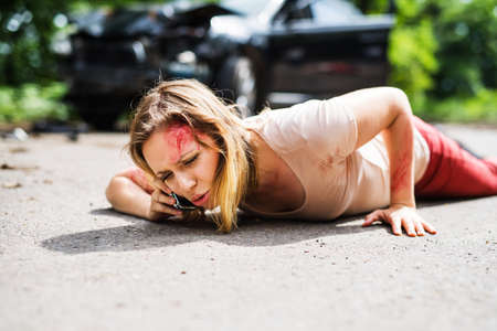 Young injured woman lying on the road after a car accident, making a phone call.の写真素材